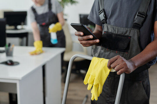 Hands of young African American male cleaner of modern cleaning service company choosing music in smartphone during work