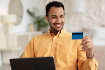 Smiling man using pc and credit card at home