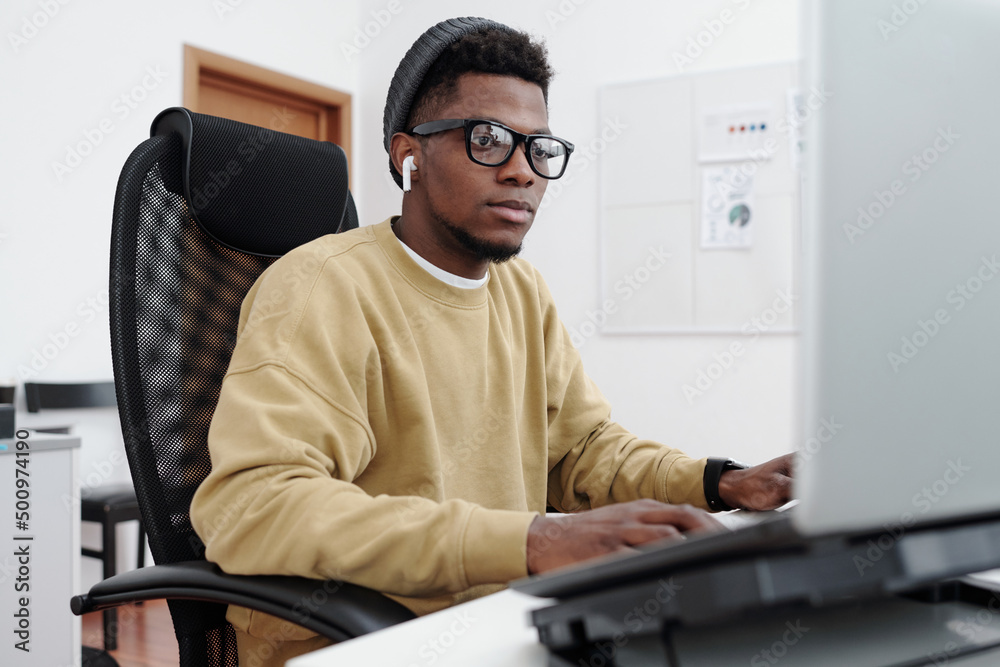 Poster young contemporary serious male it programmer in yellow sweatshirt looking at computer screen while 