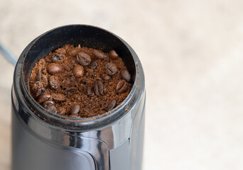 Electric automatic coffee grinder in the process of grinding roasted arabica coffee beans on a plain background