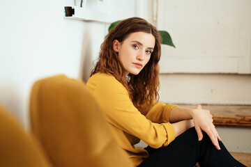 young woman with yellow blouse looks thoughtfully melancholic into camera