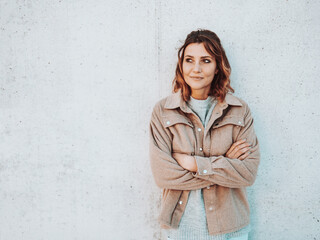 young woman stands laughing with folded arms in front of grey wall