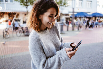 young laughing woman standing in pedestrian zone looking at her cell phone