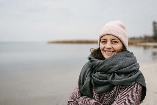 middle aged woman standing by the sea in winter with a gray scarf and looking into the camera