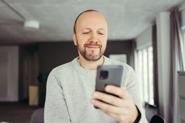 middle aged man stands in the living room and looks at his cell phone