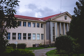 Beautiful old centuries building (now used as public university) with neoclassical style, columns and triangle roof in facade, trees, branches, grass and cloudy sky, Valdivia, Chile