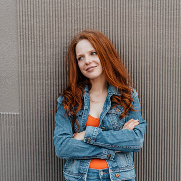 young smiling redhead woman leaning against a house wall and looking to the side