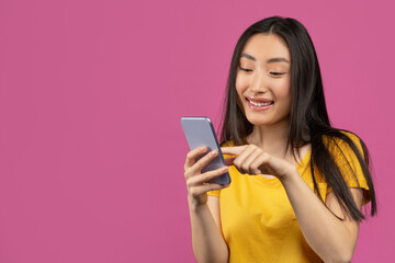 Naklejka premium Cheerful asian lady using smartphone for messaging with friends, texting on cellphone, violet background, free space