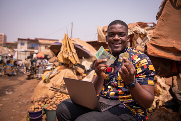 African boy at the market holding FCFA francs and a Bitcoin coin, implementation of cryptocurrencies in africa - obrazy, fototapety, plakaty