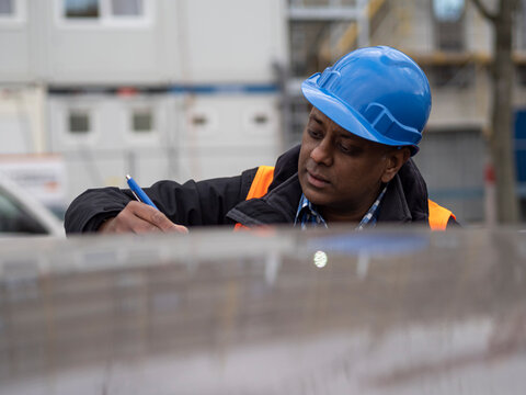 Indian engineer wearing protective workwear writing his projects and signing documents, outdoors