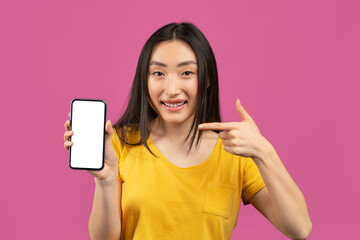 Check this out. Excited korean lady pointing at smartphone with empty screen on violet background, mockup
