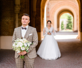 Front view of thoughtful and handsome bridegroom in elegant plaid suit, holding bouquet of flowers, looking away while waiting for first meet with bride