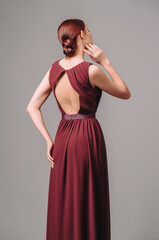 Valentine's day romantic outfit. Burgundy chic gown. Red cocktail sleeveless dress with rounded neckline and back details. Sensual young ginger lady. Studio shot.