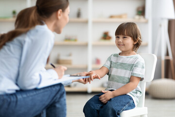 First meeting with patient. Friendly professional woman child psychologist greeting cute little boy, touching his hand - obrazy, fototapety, plakaty
