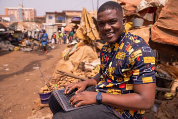 Young african boy uses his computer at the market, young people and technology in africa - obrazy, fototapety, plakaty