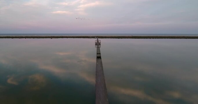 Aerial Beautiful Shot Of Birds Flying In Sky, Drone Flying Forward Over Jetty In Lake During Sunset - Djerba, Tunisia