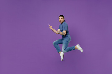 Full body side view young man 20s in basic blue t-shirt jump high point index finger aside on workspace area mock up isolated on plain purple color background studio portrait People lifestyle concept