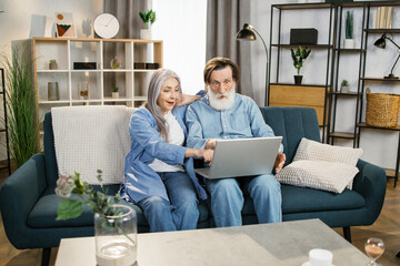Fototapeta premium Happy senior couple, happy husband overjoyed wife looking at laptop screen feel excited received fantastic news. Concept of online lottery win great commercial offer retirement and free time.