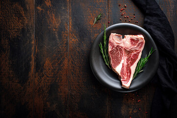 Raw t bone steak on a black plate on a wooden table. Fresh beef meat dry aged with seasonings, top...