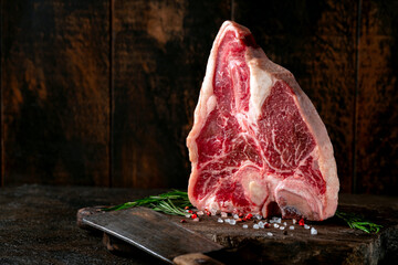 Large raw t-bone steak on a wooden board with seasonings and pepper. Fresh beef meat dry aged in a...