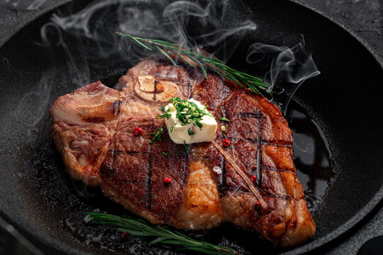 T-bone steak is fried in a grill pan with spices, butter and smoke. Premium porterhouse beef steak on the bone, close up