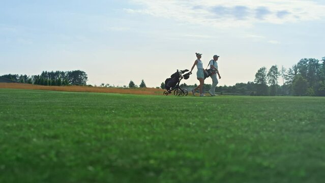 Golf players walk field on course. Golfing couple hold equipment clubs outside.