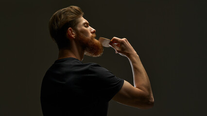 Stylish man brushing his beard and moustache. Bearded man with hair brush on black background....