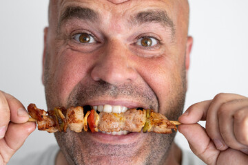 Close-up portrait of middle aged man biting a meat skewer.
