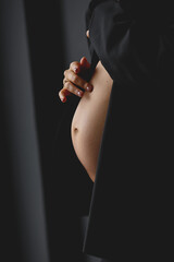 Mother gently touches the baby on stomach. Pregnant woman in black jacket touching her belly on black background. Love concept
