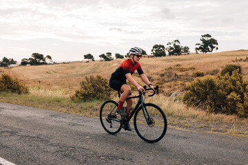 Fototapeta premium Young healthy cyclist riding a bike on countryside. Professional woman cyclist exercising.