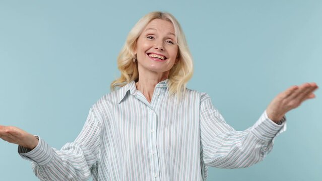 Friendly elderly gray-haired blonde woman lady 40s years old wears white shirt point index finger on camera you wave hand say come here isolated on plain pastel light blue background studio portrait