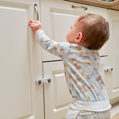 Toddler baby boy rips off a cabinet drawer with his hand. The child holds the cabinet door handle,...