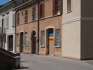 Comacchio, Italy. Old town street and building with the rainbow flag hanging on the wooden door. On the flag is the word peace, written in Italian.