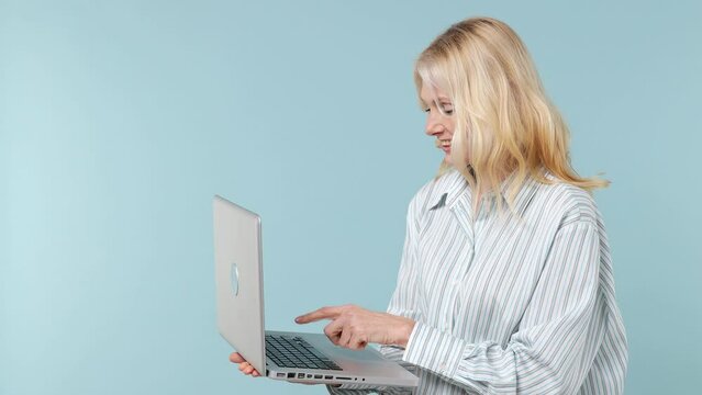 Smiling cheerful fascinating elderly gray-haired blonde woman lady 40s years old wears white shirt hold use work on laptop pc computer isolated on plain pastel light blue background studio portrait