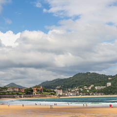 Wide sandy beach with people walking on a sunny day on the ocean coast in the Spanish city of San Sebastian