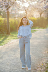 Beautiful young woman of 19 years old in light casual clothes in pastel shades near flowering sakura trees. Spring portrait of model with blue eyes.