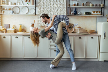 Happy millennial european woman and man dancing together in modern kitchen interior, profile