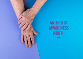 Hands of elderly woman crossed on blue and violet background. Arthritis Awareness Month concept.