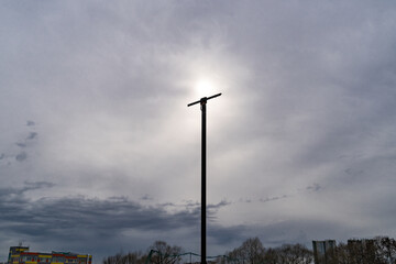 Fototapeta na wymiar The sun behind the clouds shines like a lamp on a city lighting pole.