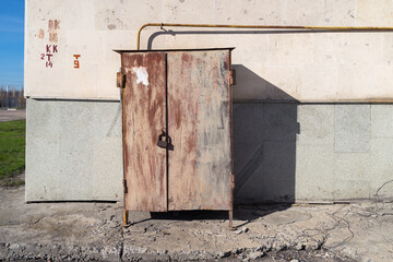 A rusty metal cabinet to cover a gas valve and a locked faucet on a city street.