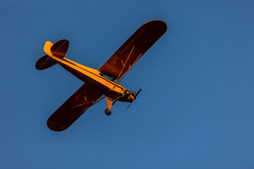 A small orange plane flying at sunset.