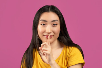 Naklejka premium Mysterious asian lady holding finger near lips and looking at camera, pretty woman making shh gesture