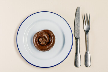 Plastic excrement lies on a plate between a fork and a knife close-up. The concept of an inept cook, fake news, shitty restaurant, bad food, taste of shit