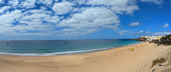 Beautiful panoramic view of long wide morro jable beach on fuerteventura island under a blue cloudy sky with less people and some boats