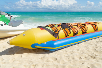 Inflatable bananas for group skating on the sea. Active rest,  attraction on the water. Banana boat with life jackets on a sandy beach against the backdrop of the sea.