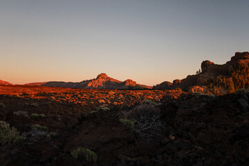 Sunset over the volcanic landscape with mountains in the background. Golden hour and warm colors over the lava and rock nature. Photo taken at the volcano Teide national park in Tenerife, Spain.