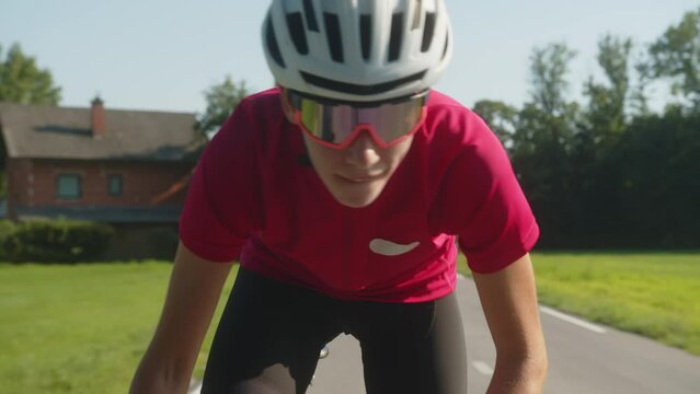 Young Caucasian female professional bicyclist during road cycling sprint, continual motion with maximal effort, close-up view.