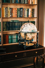 Big wooden vintage globe in a table near bookshelf in library.