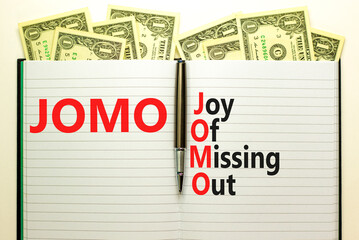 JOMO joy of missing out symbol. Concept words JOMO joy of missing out on book on beautiful white background. Dollar bills. Business JOMO joy of missing out concept. Copy space.