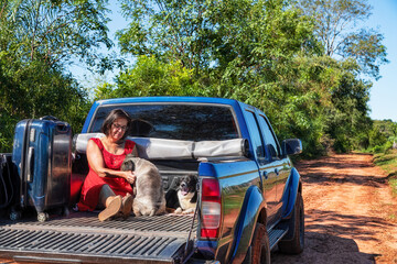 A woman sitting in the back of a pickup truck with her dogs and suitcase, all on a typical red sand...